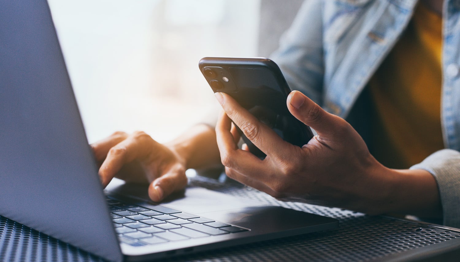 Female holding her mobile phone while looking at her laptop